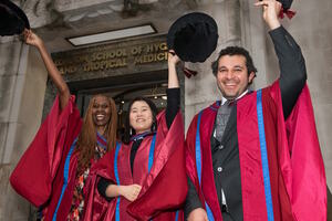 A group of three doctoral graduates in regalia and waving their bonnets.