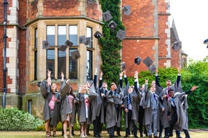 Students from the University of York standing outside a red-brick university building and throwing their mortarboard hats.