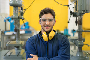 a young man working in STEM standing in a factory wearing protective glasses and yellow ear muffs